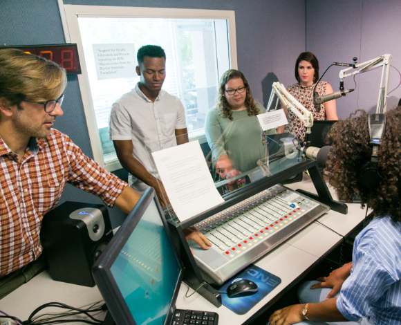 An instructor points to a sound board as students gather around